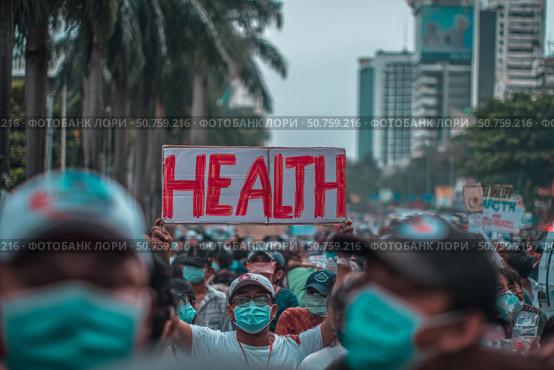 Crowd of masked protesters holding health sign in urban area. Стоковое AI-изображение, AI-художник Мария Фадеева / Фотобанк Лори