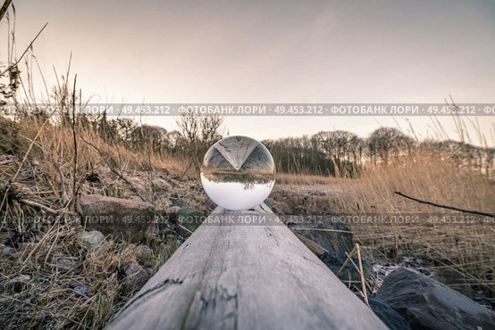 Crystal ball in balance on a wooden log in the nature by a lake. Стоковое фото, агентство Ingram Publishing / Фотобанк Лори