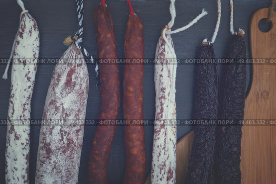 Cured meat and sausages hanging on black wooden background close up, retro toned. Cured meat and sausages. Стоковое фото, агентство Ingram Publishing / Фотобанк Лори