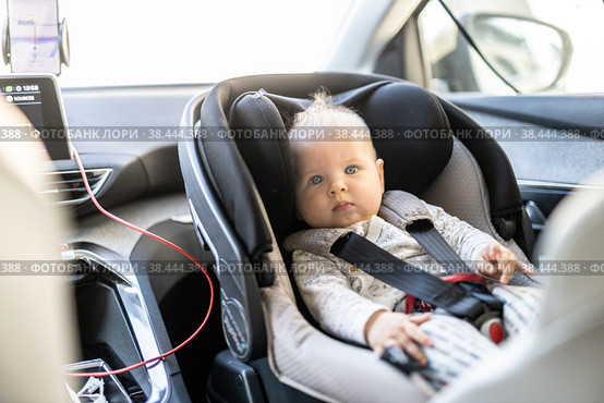 Cute little baby boy strapped into infant car seat in passenger compartment during car drive. Стоковое фото, фотограф Matej Kastelic / Фотобанк Лори