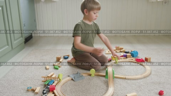 Cute little blonde child boy sitting on the floor playing with wooden toy train. Toddler kid plays railway. Made of natural materials. Birthday gift. Preschool employment. Brain, coordination exercise. Стоковое видео, видеограф Марина Демидюк / Фотобанк Лори