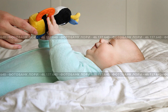 Cute Newborn Baby Lying on the Back and Plays with Colorful Toys. Little Three Month Child Takes a Toy. Portrait of Playful Neonate Toddler. Concept of Childhood, New Life, Baby Care. Top View. Стоковое фото, фотограф Марина Демидюк / Фотобанк Лори