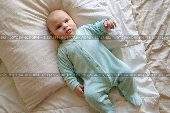 Cute Newborn Baby Lying on the Back in a Child Crib on White. Top View of Little Energetic Child. Playful Neonate Toddler Looks Around and Waving Hands. Concept of Childhood, New Life, Baby Care. Стоковое фото, фотограф Марина Демидюк / Фотобанк Лори