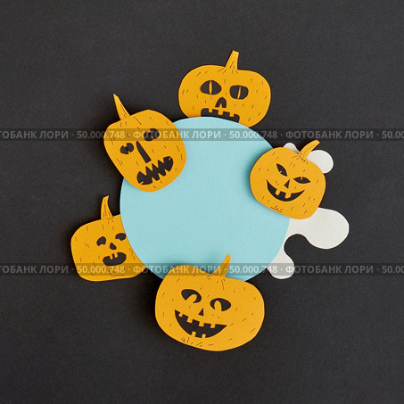 Decorative application handcraft from paper with terrible yellow pumpkins smiling on a blue round frame on a black background, place for text. Halloween concept. Flat lay.. Creative Halloween handmade blue frame with paper horrible smiling and laughing pumpkins on a black paper background. Стоковое фото, агентство Ingram Publishing / Фотобанк Лори