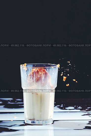 Delicious biscuit in a glass of milk and spilled milk on a black wooden background with copy space. Traditional Christmas treat for Santa - homemade oatmeal cookies.. Homemade peanut cake fall to a glass of milk with splash on a black wooden table. Стоковое фото, агентство Ingram Publishing / Фотобанк Лори