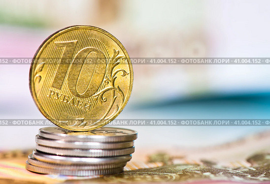 Деньги. Монета номиналом в 10 рублей на стопке монет в 1 рубль. На фоне 100-рублевых купюр. Стоковое фото, фотограф E. O. / Фотобанк Лори