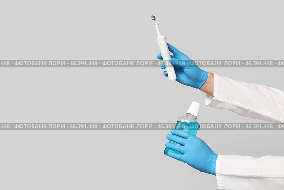 Dentist hands with electric toothbrush and bottle of mouth rinse on grey background. World Dentist Day. Стоковое фото, фотограф Pixel_shot / Фотобанк Лори