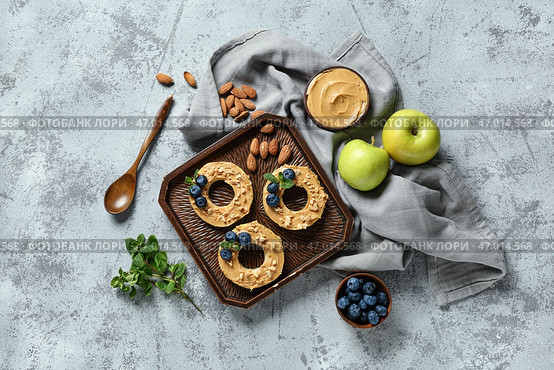 Деревянный поднос с вкусными яблочными кружочками, миска с ореховой пастой, черникой и миндалем на сером грубом фоне. Стоковое фото, фотограф Pixel_shot / Фотобанк Лори