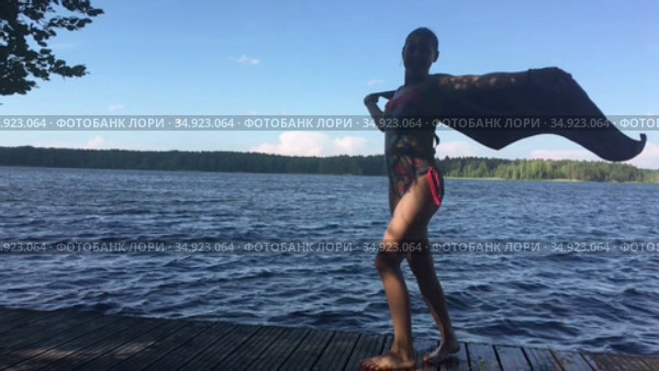 Девочка стоит на причале с развевающимся на ветру полотенцем, замедленное видео. Стоковое видео, видеограф Кекяляйнен Андрей / Фотобанк Лори