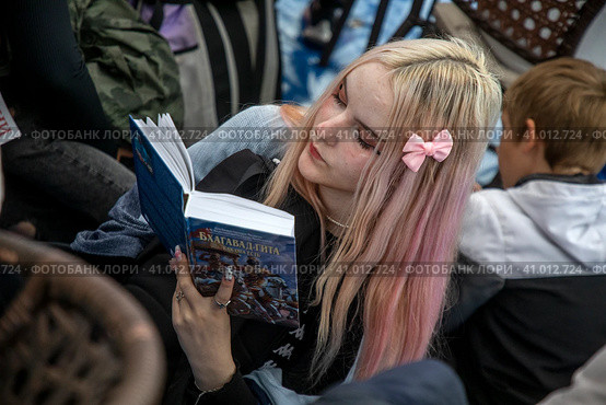 Девушка читает книгу с текстом индуистского священного писания "Бхагавадгита" на площадке фестиваля День Индии в городе Москве, Россия (2023 год). Редакционное фото, фотограф Николай Винокуров / Фотобанк Лори