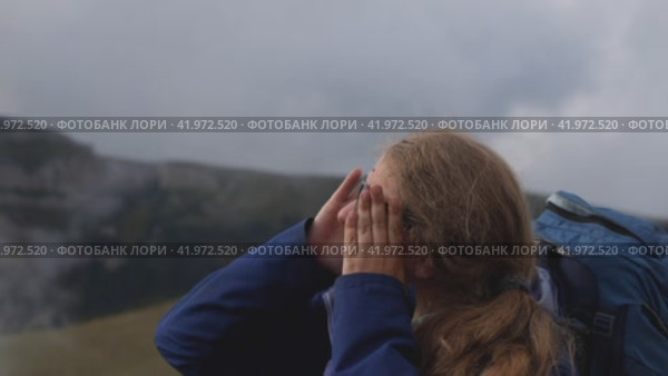 Девушка-туристка надевает солнцезащитные очки. За спиной у нее висит рюкзак. На заднем плане гора в облаках. Концепция горного туризма. Стоковое видео, видеограф Воловодов Владимир / Фотобанк Лори