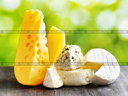 Different types of cheese on a black wooden table and on nature background. Maasdam cheese, Brie, Parmesan cheese, Gouda and blue cheese Roquefort. Organic healthy food rich in calcium and minerals. Стоковое фото, агентство Ingram Publishing / Фотобанк Лори