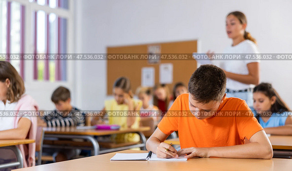 Diligent tween boy making notes of teacher lecture in class. Стоковое фото, фотограф Яков Филимонов / Фотобанк Лори