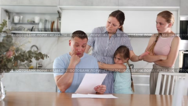 Disgruntled father carefully reads documents. Whole family stands in fear in the background. Стоковое видео, видеограф Яков Филимонов / Фотобанк Лори