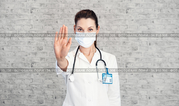 Doctor woman makes stopping hand gesture. Girl Doctor wearing protection face mask against covid-19. Banner panorama medical staff preventive gear about coronavirus. Woman in medical mask stops nCov. Стоковое фото, фотограф Сергей Тимофеев / Фотобанк Лори