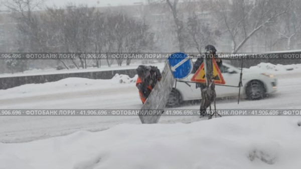 Дорожные рабочие устанавливают знаки объезда на городской трассе. Сильный снегопад в городе. Автомобили едут по заснеженной дороге. Москва, Россия, 3 декабря 2023. Редакционное видео, видеограф Ирина / Фотобанк Лори