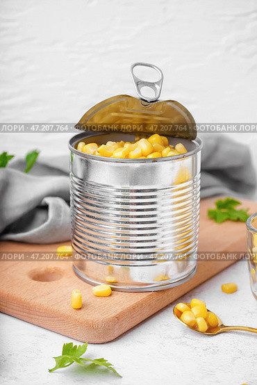 Доска с консервной банкой, кукурузными зернами и листьями петрушки на сером столе. Стоковое фото, фотограф Pixel_shot / Фотобанк Лори