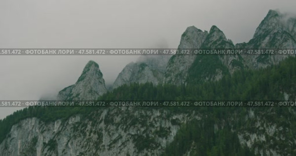 Dramatic mountain peaks covered in mist with green forests below under an overcast sky. Стоковое видео, видеограф Ольга Сухарева / Фотобанк Лори