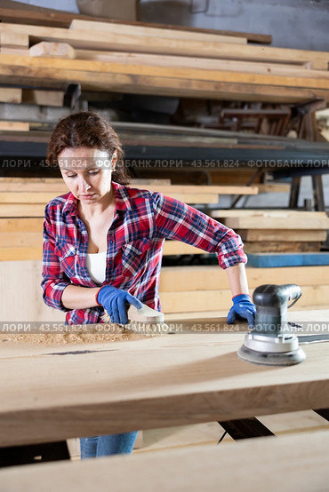 During manufacturing, woman employee grinds surface of wooden board, gives smoothness to surface. Стоковое фото, фотограф Яков Филимонов / Фотобанк Лори