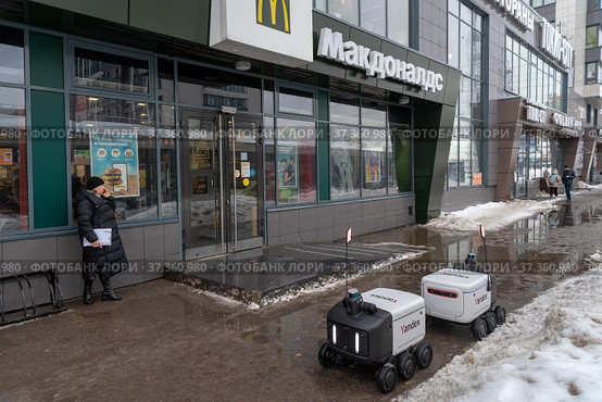 Два ровера доставки еды «Яндекс» возле ресторана «Макдоналдс» (McDonald’s). Город Мурино Всеволожского района Ленинградской области (2022 год). Редакционное фото, фотограф Румянцева Наталия / Фотобанк Лори