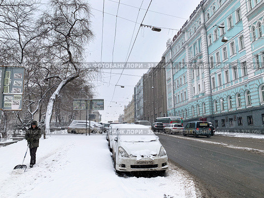 Дворник с лопатой и занесенная снегом машина на Светланской улице во Владивостоке в период мартовского циклона (2020 год). Редакционное фото, фотограф Овчинникова Ирина / Фотобанк Лори