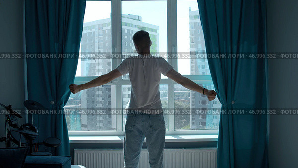 Early morning, silhouette of man exercising, stretching body by window at home. Стоковое фото, фотограф David Kashakhi / Фотобанк Лори
