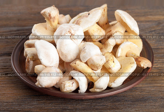 Edible wild mushrooms on a wooden background. Forest cleaned mushrooms in a clay plate. Стоковое фото, агентство Ingram Publishing / Фотобанк Лори