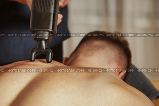 Effective Sports Massage Using Percussion Massager in a Relaxing Indoor Setting. Стоковое фото, фотограф Aleksandr Golubev / Фотобанк Лори