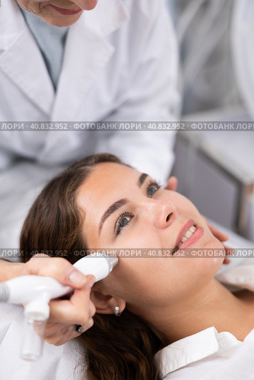 Elderly female beautician doing procedure of microneedling, mesotherapy for young woman in beauty salon indoors. Стоковое фото, фотограф Яков Филимонов / Фотобанк Лори