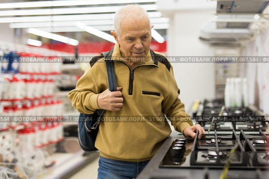 elderly grayhaired man pensioner looking gas hob at counter in showroom of electrical appliance hypermarket department. Стоковое фото, фотограф Татьяна Яцевич / Фотобанк Лори