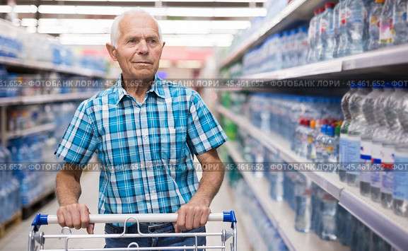 elderly retired man buying bottle of drinking water in alcohol section of supermarket. Стоковое фото, фотограф Татьяна Яцевич / Фотобанк Лори