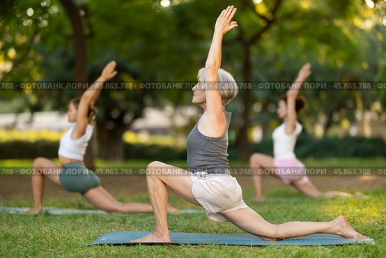 Elderly woman performing Anjaneyasana during group yoga training in park. Стоковое фото, фотограф Яков Филимонов / Фотобанк Лори