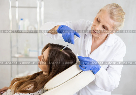 Elderly woman trichologist doing injections into female patient scalp. Стоковое фото, фотограф Яков Филимонов / Фотобанк Лори