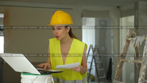 emale foreman in a protective helmet and a yellow vest checks the execution of repair work using a laptop. Стоковое видео, видеограф Яков Филимонов / Фотобанк Лори