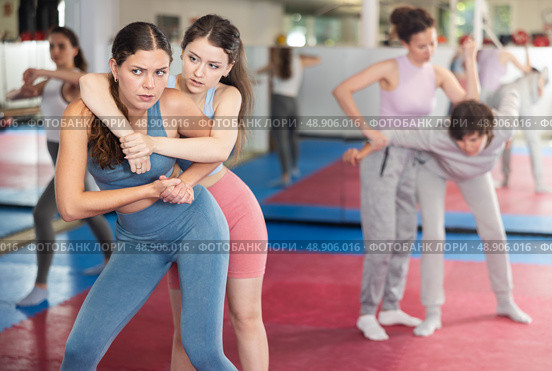 Emotional woman trying to escape from back grip and delivering elbow strike to midsection to female opponent during mock bout in self defense training. Стоковое фото, фотограф Яков Филимонов / Фотобанк Лори
