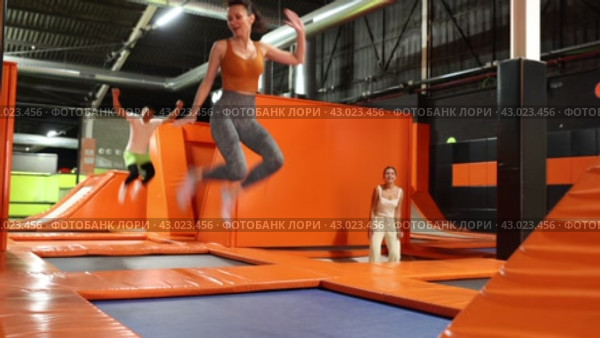 Enthusiastic middle-aged woman experiencing thrill of leaping high at vibrant trampoline gym with friends. Стоковое видео, видеограф Яков Филимонов / Фотобанк Лори
