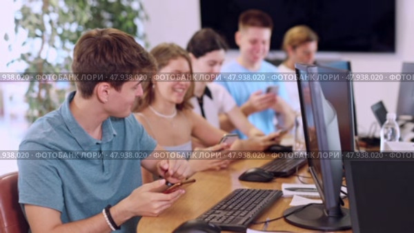 Enthusiastic young guy undergoing training in mobile applications development, sitting at table with computer and using smartphone to test app prototype. Стоковое видео, видеограф Яков Филимонов / Фотобанк Лори