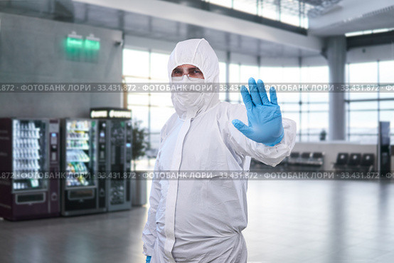 Epidemiologist in a protective suit shows a prohibition gesture against the waiting room at the airport or train station. Стоковое фото, фотограф Евгений Харитонов / Фотобанк Лори