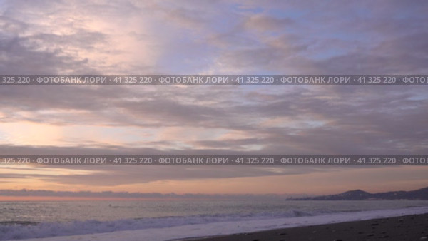 Evening. Sea. The sky is painted in pastel shades of pink and blue. The cape and city buildings are visible in the distance. Waves foaming on a pebble beach. A husky dog runs along the shore and hides. Стоковое видео, видеограф Вера Ивановна Кубарева / Фотобанк Лори