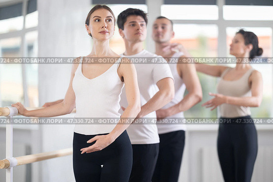 Experience female ballet instructor adjusting students form. Diligent girls and boys practice ballet movements near ballet barre in dancing hall. Стоковое фото, фотограф Яков Филимонов / Фотобанк Лори