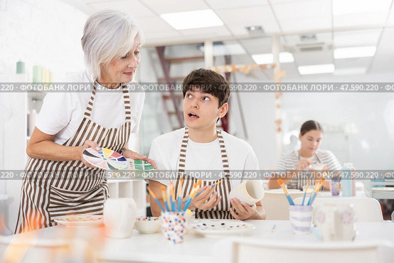 Experienced female ceramicist teaching enthusiastic guy to paint pottery. Стоковое фото, фотограф Яков Филимонов / Фотобанк Лори