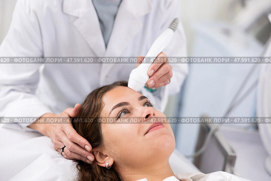 Faceless cosmetologist doing facial skin ultrasound cavitation for flawless woman face in beauty salon. Стоковое фото, фотограф Яков Филимонов / Фотобанк Лори