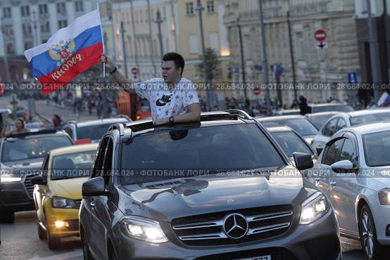 Фанат с российским флагом вылез из люка автомобиля после матча Россия-Испания в центре Москвы (2018 год). Редакционное фото, фотограф Дмитрий Неумоин / Фотобанк Лори