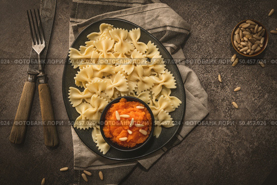 Farfalle pasta in a ceramic plate with pumpkin puree and pine nuts in a small ceramic bowl on a dark stone kitchen counter top. Стоковое фото, агентство Ingram Publishing / Фотобанк Лори