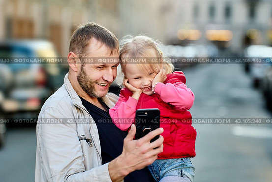 Father and smiling daughter watch on screen of handy outdoors. Стоковое фото, фотограф Владимир Григорьев / Фотобанк Лори