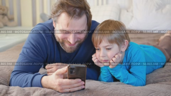 Father and son little boy laughing and using phone. They watching funny videos together, playing games on smartphone. Concept technology, smartphone addicted. Fun weekend activity. Modern fatherhood. Стоковое видео, видеограф Марина Демидюк / Фотобанк Лори