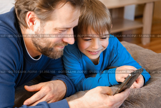 Father and son little boy laughing and using phone. They watching funny videos together, playing games on smartphone. Concept technology, smart phone addicted. Fun weekend activity. Modern fatherhood. Стоковое фото, фотограф Марина Демидюк / Фотобанк Лори