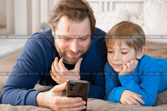 Father and son little boy laughing and using phone. They watching funny videos together, playing games on smartphone. Concept technology, smart phone addicted. Fun weekend activity. Modern fatherhood. Стоковое фото, фотограф Марина Демидюк / Фотобанк Лори