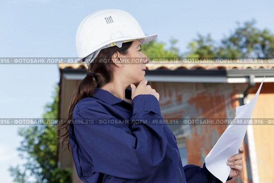 female builder wearing overalls stood outside a property holding paperwork. Стоковое фото, агентство Ingram Publishing / Фотобанк Лори