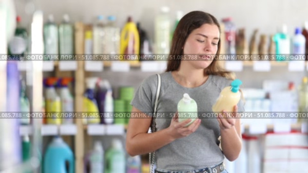 Female buyer holds liquid soap from different manufacturers in her hands and chooses between them while standing in a supermarket. Beautiful brunette girl buys antibacterial cream soap. Стоковое видео, видеограф Яков Филимонов / Фотобанк Лори